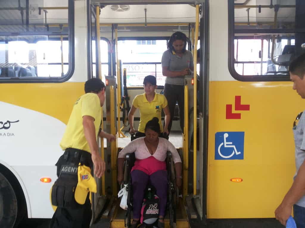 Cadeirante é auxiliada por agentes, na descida de ônibus 