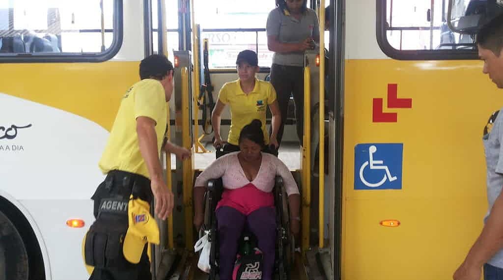 Cadeirante é auxiliada por agentes, na descida de ônibus