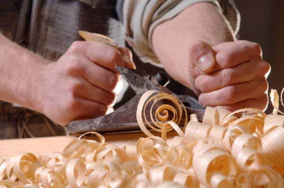 Artesão passa uma plaina manual sobre peça trabalhada